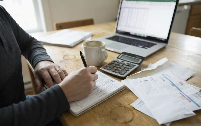 A person reviewing a household budget and unemployment paperwork at a kitchen table, mortgage statement visible